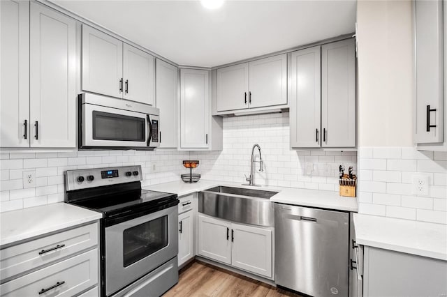 kitchen with light wood finished floors, gray cabinets, a sink, stainless steel appliances, and light countertops