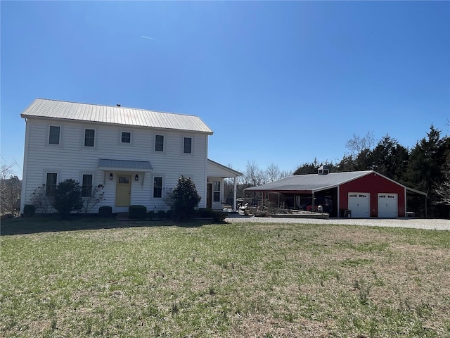 colonial-style house featuring gravel driveway, metal roof, a detached garage, and a front lawn