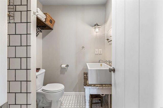 bathroom featuring toilet, a sink, tile patterned flooring, and baseboards