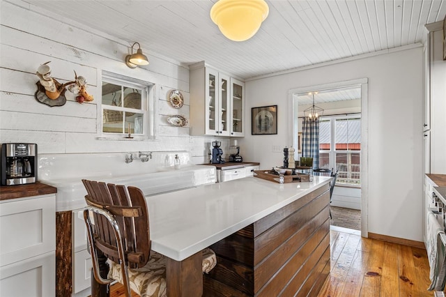 kitchen with white cabinets, light wood finished floors, a breakfast bar, baseboards, and glass insert cabinets