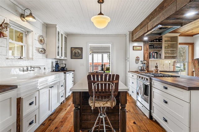 kitchen with stainless steel gas stove, open shelves, butcher block countertops, wood-type flooring, and glass insert cabinets