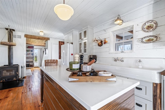 kitchen with glass insert cabinets, white cabinetry, dark wood-style floors, a wood stove, and white refrigerator with ice dispenser