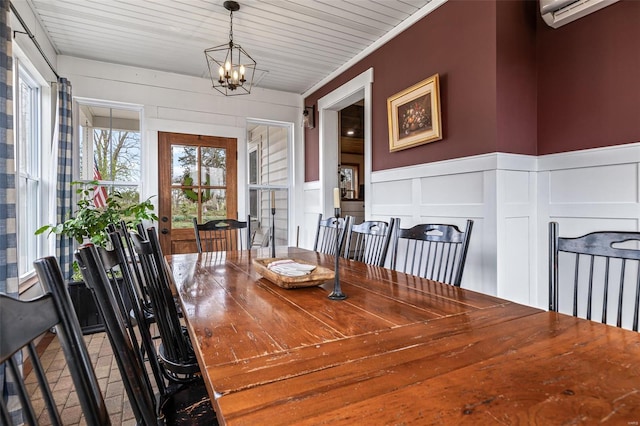 dining space with a decorative wall, wainscoting, brick floor, a wall unit AC, and a notable chandelier