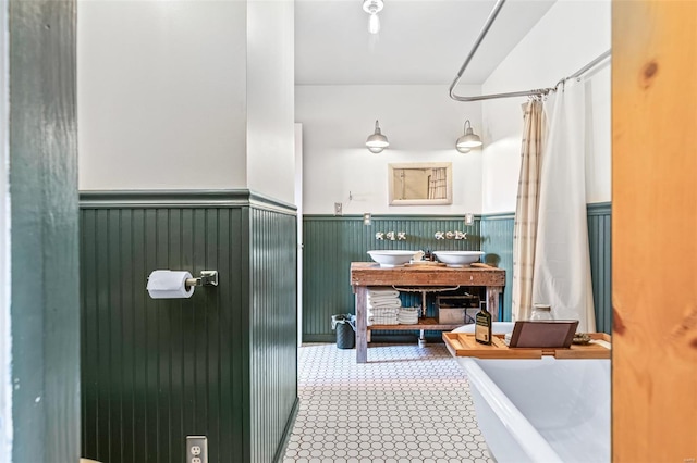 full bath featuring tile patterned floors, a freestanding tub, a shower with shower curtain, and wainscoting
