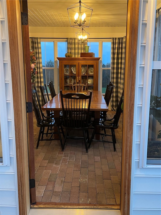 dining area with brick floor, an inviting chandelier, and wooden ceiling