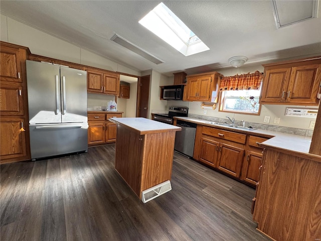 kitchen with lofted ceiling with skylight, light countertops, appliances with stainless steel finishes, brown cabinetry, and a sink