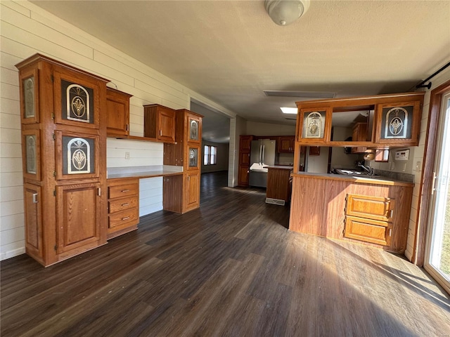 kitchen with dark wood finished floors, a peninsula, open shelves, freestanding refrigerator, and built in desk