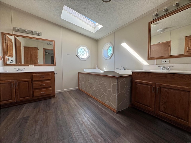 bathroom featuring lofted ceiling with skylight, two vanities, wood finished floors, and a textured ceiling