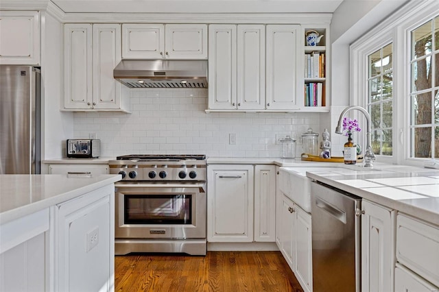 kitchen with dark wood-type flooring, under cabinet range hood, light countertops, white cabinets, and stainless steel appliances