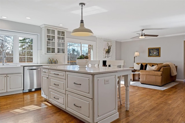 kitchen with a sink, a kitchen breakfast bar, stainless steel dishwasher, white cabinetry, and light wood-style floors