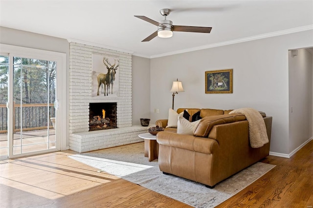 living room with wood finished floors, baseboards, a fireplace, ornamental molding, and ceiling fan