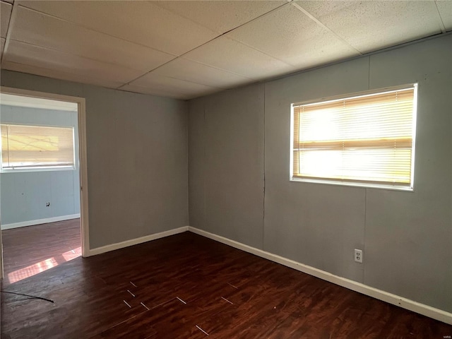 empty room featuring dark wood finished floors, a drop ceiling, and baseboards