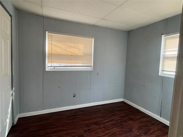 unfurnished room with wood finished floors, baseboards, and a paneled ceiling