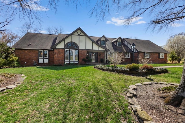 tudor-style house featuring a front lawn, a shingled roof, stucco siding, and brick siding