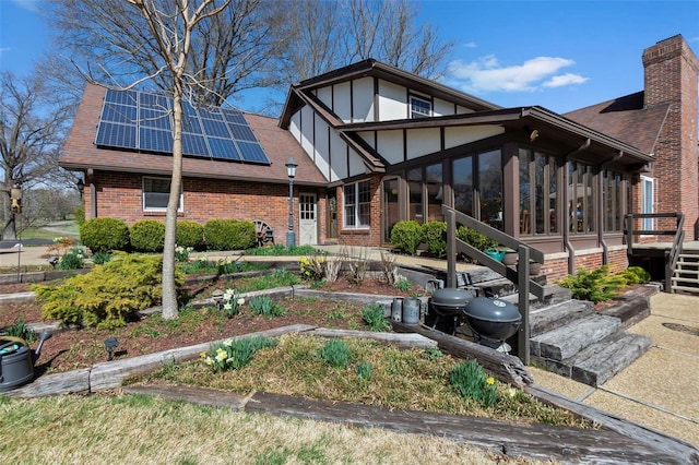tudor-style house with brick siding, a sunroom, solar panels, and roof with shingles
