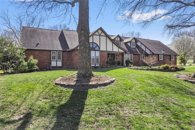 tudor house with a shingled roof, a front yard, and brick siding