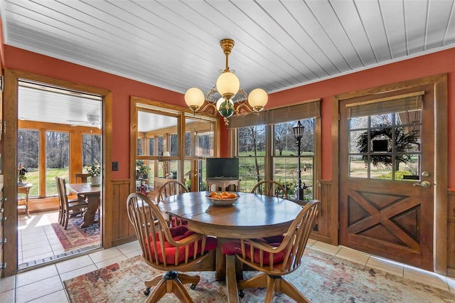 dining area with light tile patterned flooring, a healthy amount of sunlight, a chandelier, and wainscoting