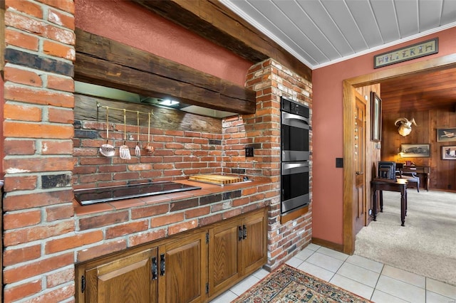 kitchen featuring light tile patterned flooring, wooden walls, crown molding, double oven, and brown cabinetry