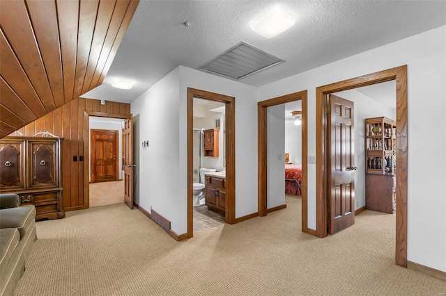 hallway featuring lofted ceiling, baseboards, a textured ceiling, wooden walls, and light carpet