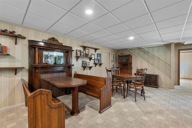 dining room with wooden walls, baseboards, stairway, a paneled ceiling, and light colored carpet