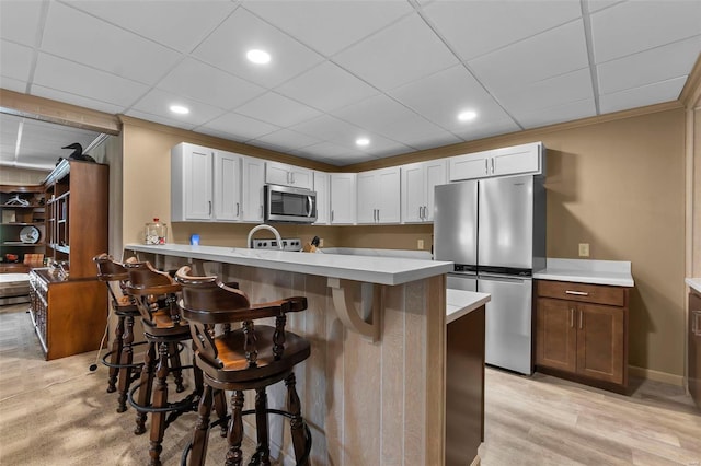 kitchen featuring light countertops, a breakfast bar, a peninsula, stainless steel appliances, and light wood-style floors