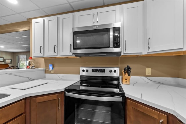 kitchen featuring range with electric cooktop, stainless steel microwave, white cabinets, and light stone counters