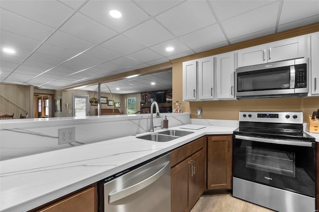 kitchen featuring light wood finished floors, a sink, stainless steel appliances, and light stone counters