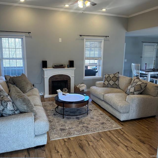 living area with a ceiling fan, wood finished floors, recessed lighting, a fireplace, and crown molding