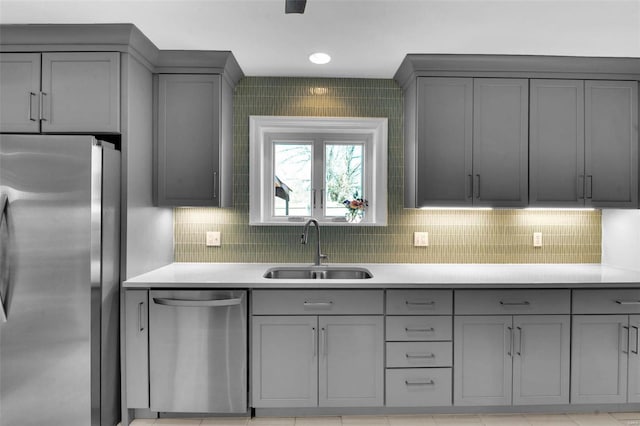 kitchen featuring a sink, gray cabinetry, light countertops, decorative backsplash, and stainless steel appliances