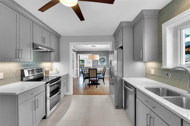 kitchen featuring under cabinet range hood, gray cabinetry, appliances with stainless steel finishes, and a sink