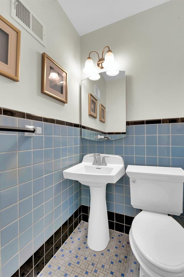 half bathroom with tile patterned flooring, visible vents, a wainscoted wall, toilet, and tile walls