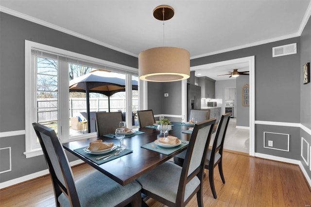 dining space featuring visible vents, baseboards, wood finished floors, and crown molding