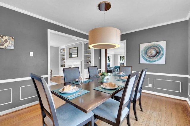 dining room with a wainscoted wall, ornamental molding, built in features, a fireplace, and light wood finished floors