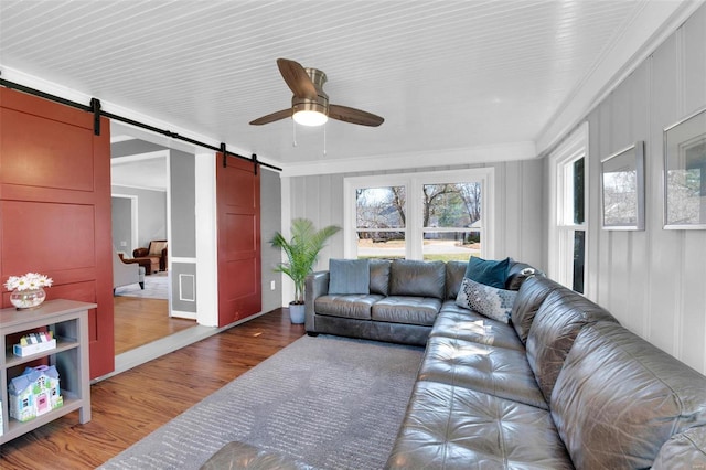 living room featuring a barn door, crown molding, wood finished floors, and ceiling fan