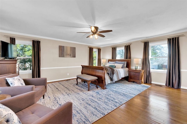 bedroom featuring wood finished floors, baseboards, visible vents, ceiling fan, and crown molding