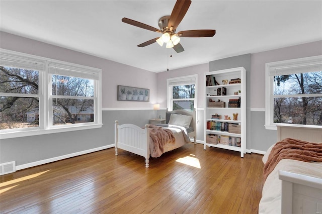 bedroom with hardwood / wood-style floors, visible vents, baseboards, and a ceiling fan