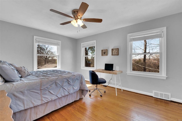 bedroom with multiple windows, wood finished floors, visible vents, and baseboards