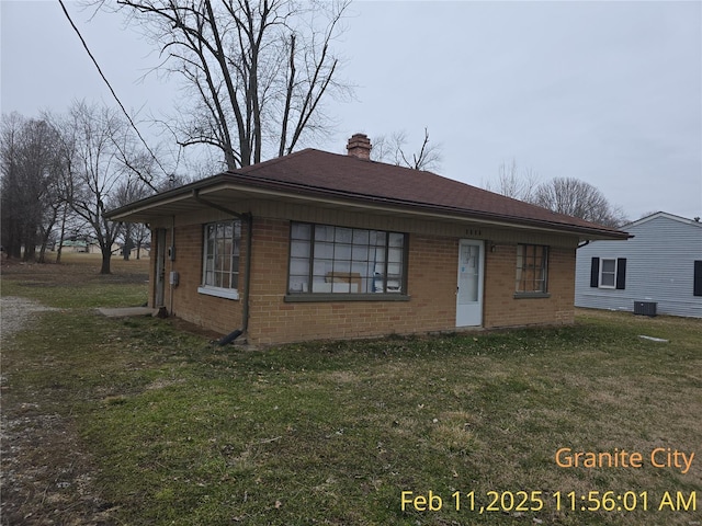 view of front of home with central air condition unit, brick siding, a chimney, and a front yard