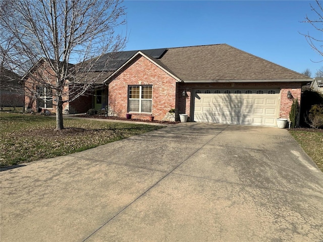 ranch-style home featuring driveway, roof with shingles, an attached garage, brick siding, and solar panels