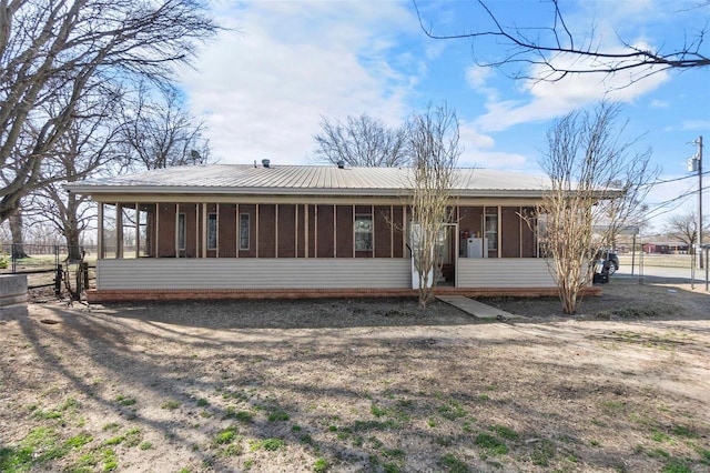 rear view of property featuring metal roof, fence, brick siding, and a sunroom