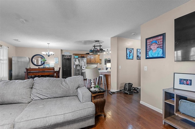 living area with an inviting chandelier, dark wood-style floors, baseboards, and a textured ceiling