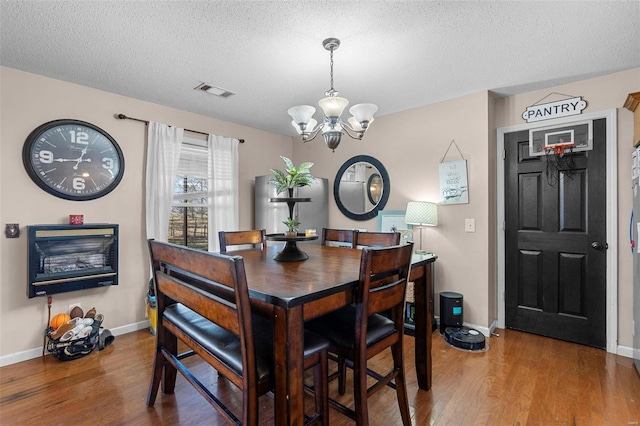 dining space featuring visible vents, a textured ceiling, an inviting chandelier, and wood finished floors