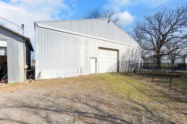 view of pole building with a trampoline, fence, a yard, and driveway