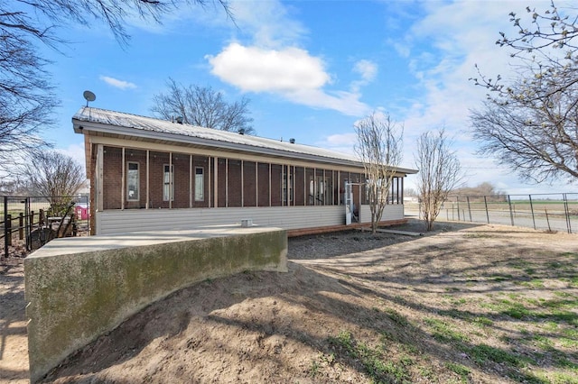 rear view of house with fence, brick siding, a sunroom, and metal roof