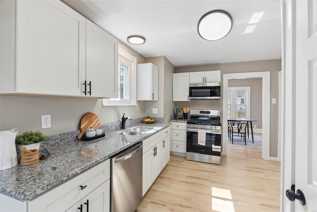 kitchen featuring light stone countertops, light wood-style flooring, a sink, appliances with stainless steel finishes, and white cabinetry