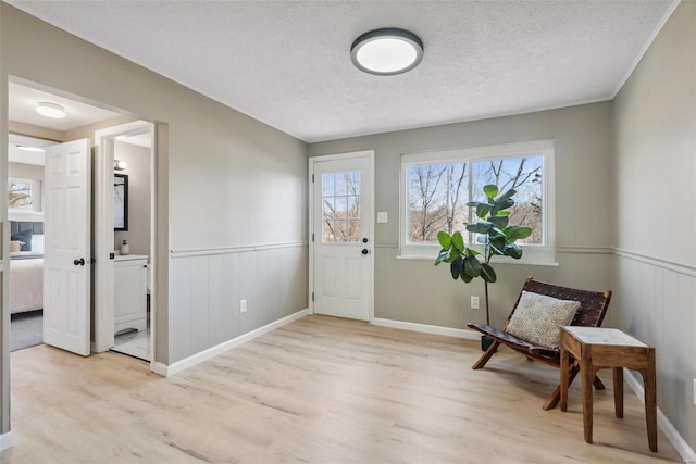 entrance foyer with light wood-type flooring, a textured ceiling, and wainscoting