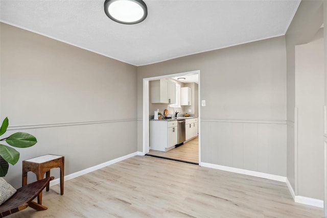 sitting room with light wood-type flooring, baseboards, a textured ceiling, and wainscoting