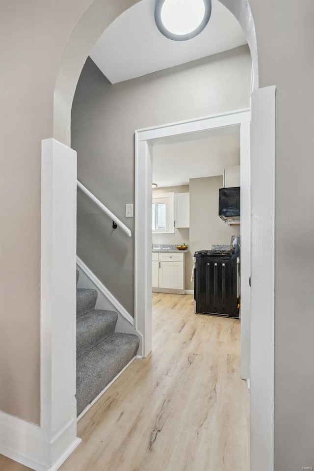 hallway with arched walkways, stairway, light wood-style flooring, and baseboards