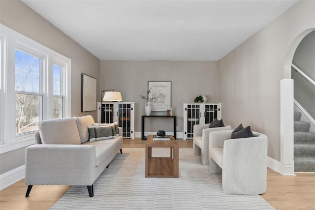 living room featuring arched walkways, light wood-style flooring, stairs, and baseboards