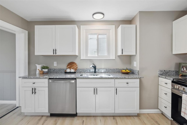 kitchen with light wood finished floors, light stone countertops, appliances with stainless steel finishes, white cabinets, and a sink